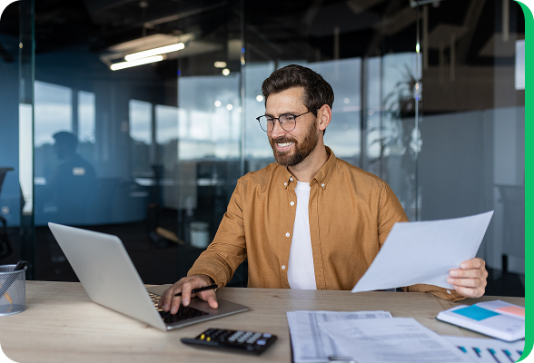 Smiling man working on a laptop in a modern office, comparing energy contracts online.